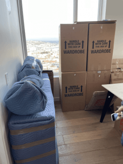 Furniture wrapped in padding and moving boxes stacked by a window